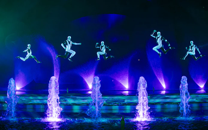 Performers in mid-air during the Kiss of the Sea Show with illuminated fountains.