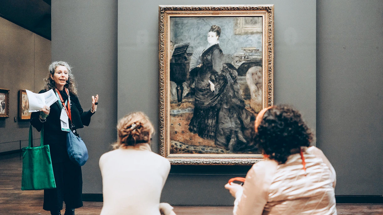 Guide explaining painting to tourists inside Orsay Museum, Paris.