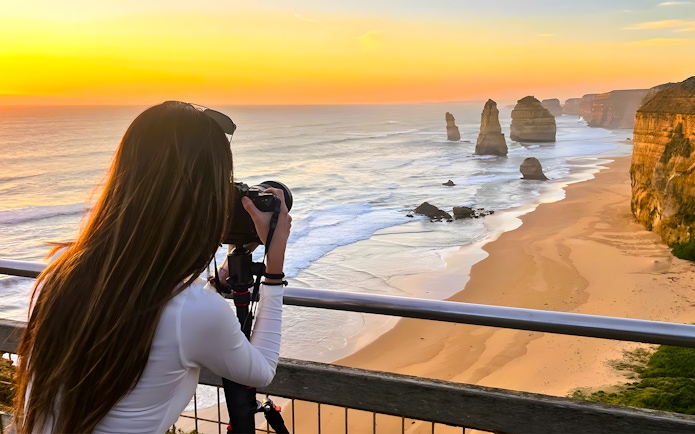 Tourist photographing the 12 Apostles at sunset on the Great Ocean Road.