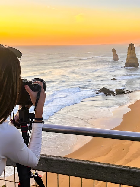 Tourist photographing the 12 Apostles at sunset on the Great Ocean Road.