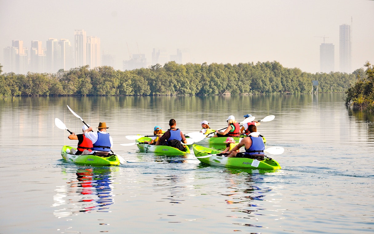 Kayakers paddling through mangroves with Abu Dhabi skyline in the background.