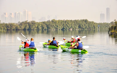Kayakers paddling through mangroves with Abu Dhabi skyline in the background.