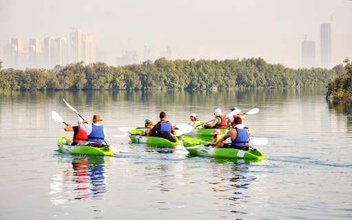 Kayakers paddling through mangroves with Abu Dhabi skyline in the background.