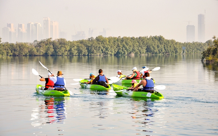 Kayakers paddling through mangroves with Abu Dhabi skyline in the background.