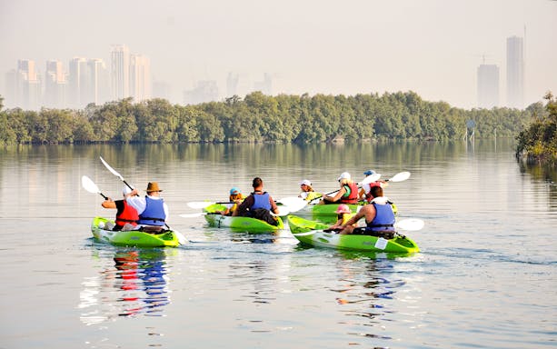 Kayakers paddling through mangroves with Abu Dhabi skyline in the background.