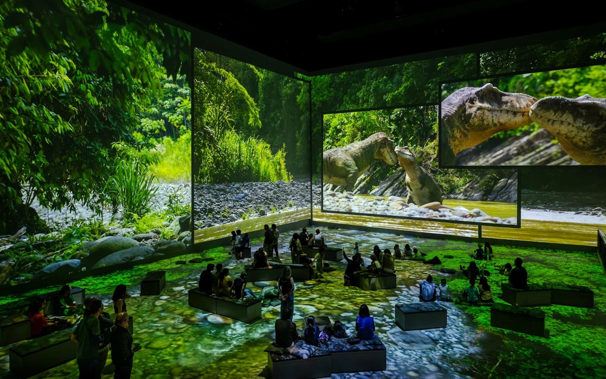 Dinosaurs projected in a lush forest setting at Atelier Des Lumières, Paris exhibition.