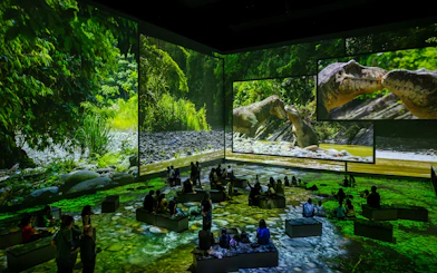 Dinosaurs projected in a lush forest setting at Atelier Des Lumières, Paris exhibition.
