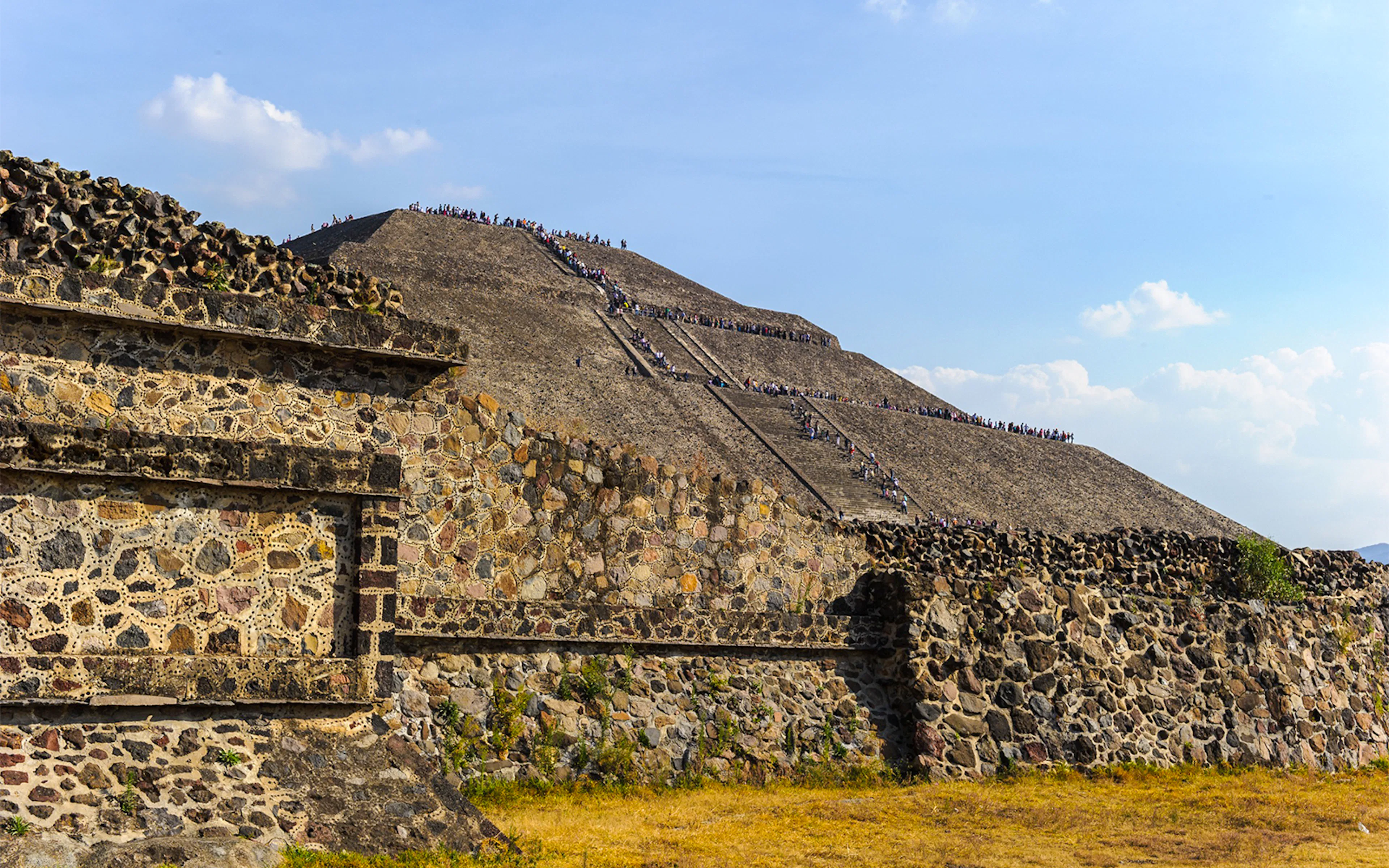 Pyramid of the Sun in Teotihuacan, Mexico, with visitors climbing the ancient stone steps.