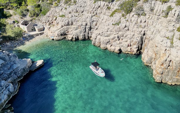 Boat in clear waters of Mala Stiniva bay surrounded by rocky cliffs.