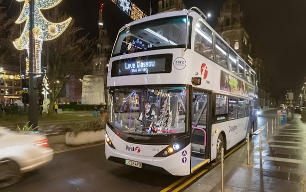 Double-decker bus in Glasgow city center at night, offering airport transfer service.