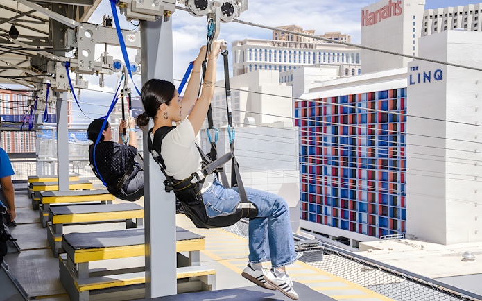 People ziplining at Fly LINQ Zipline with Las Vegas skyline in the background.