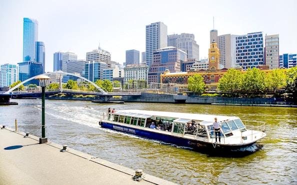 Melbourne River Cruises boat on Yarra River with city skyline in background.