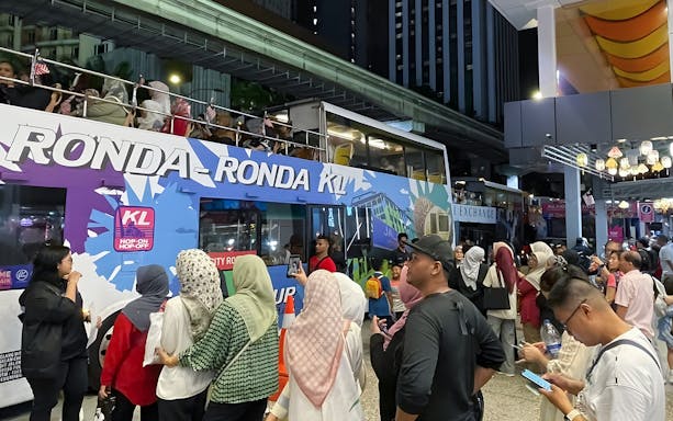 Crowd boarding Kuala Lumpur Hop-On Hop-Off night bus under city lights.