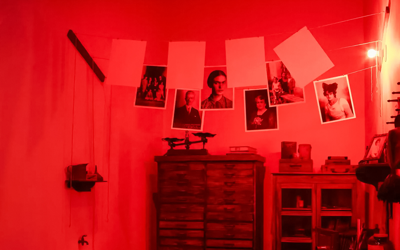 Photographs hanging in a red-lit traditional darkroom.