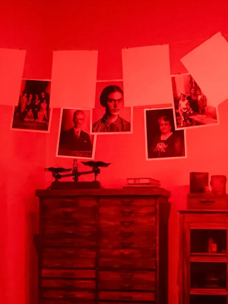 Photographs hanging in a red-lit traditional darkroom.