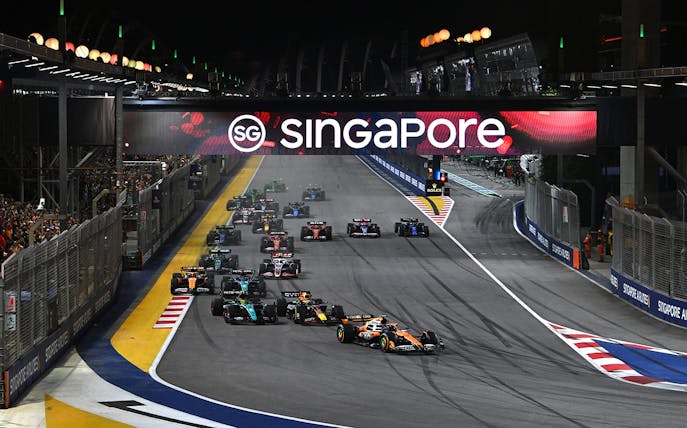Formula 1 cars racing at night under Singapore sign during F1 Singapore Grand Prix.