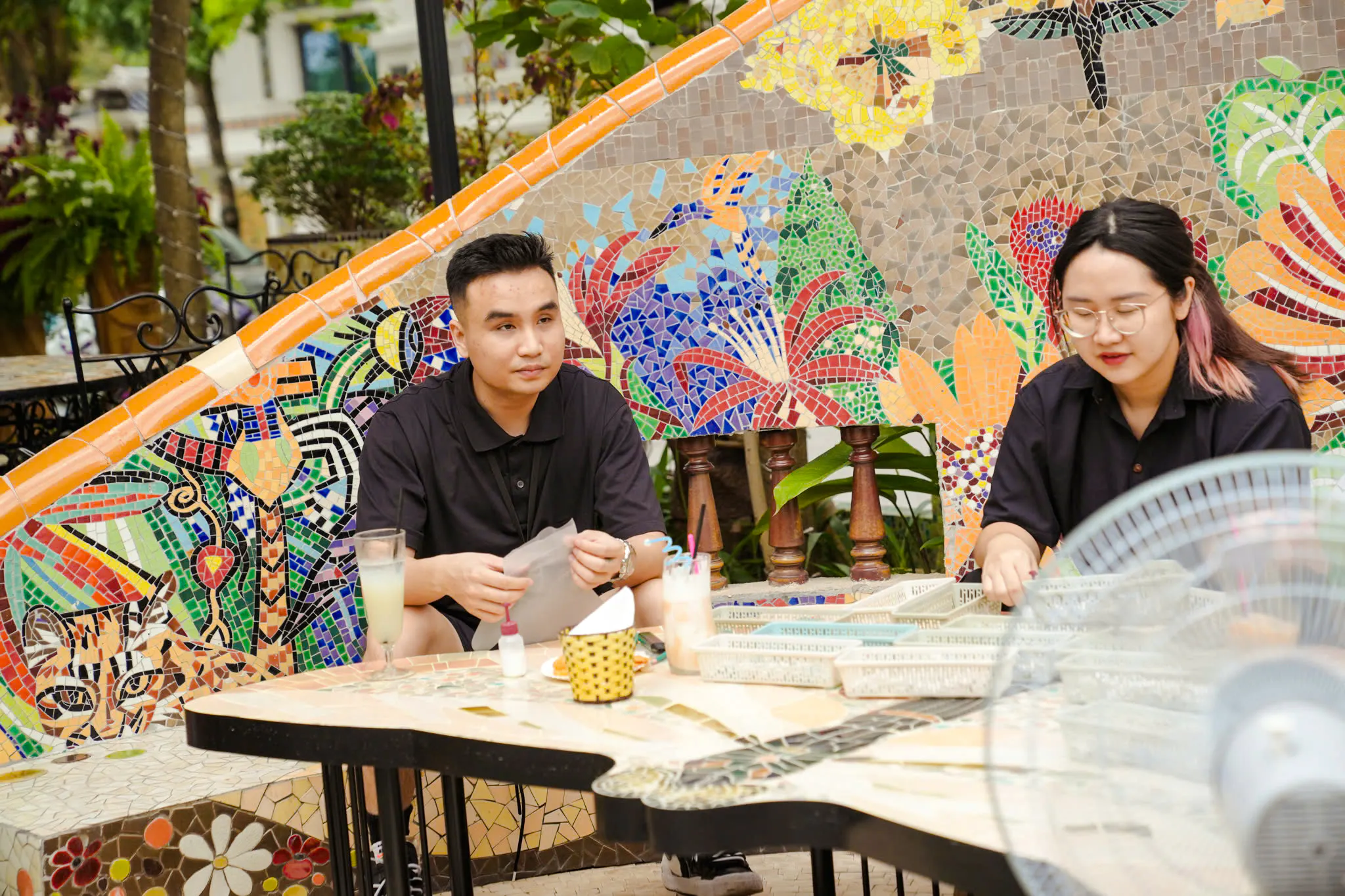 Crafting mosaics at Pottery Village, Ha Noi, with colorful tile designs in the background.