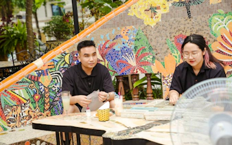 Crafting mosaics at Pottery Village, Ha Noi, with colorful tile designs in the background.