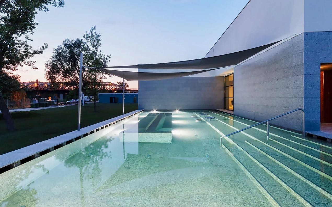 Indoor pool at Pesterzsebet Bath, Budapest with modern architecture and evening lighting.