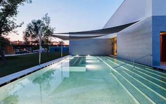 Indoor pool at Pesterzsebet Bath, Budapest with modern architecture and evening lighting.