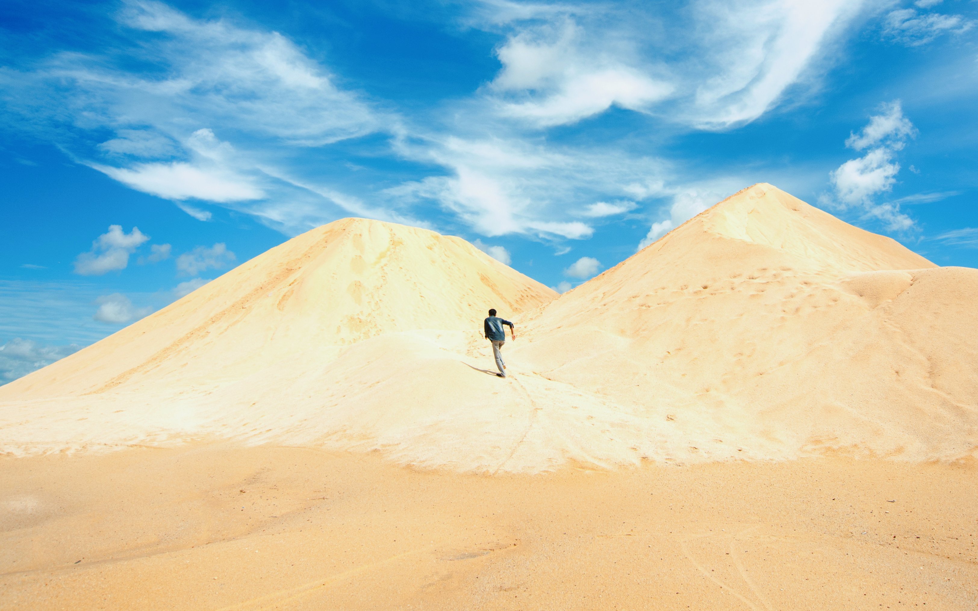 Person walking on sand dunes in the mini desert of Bintan under a blue sky.