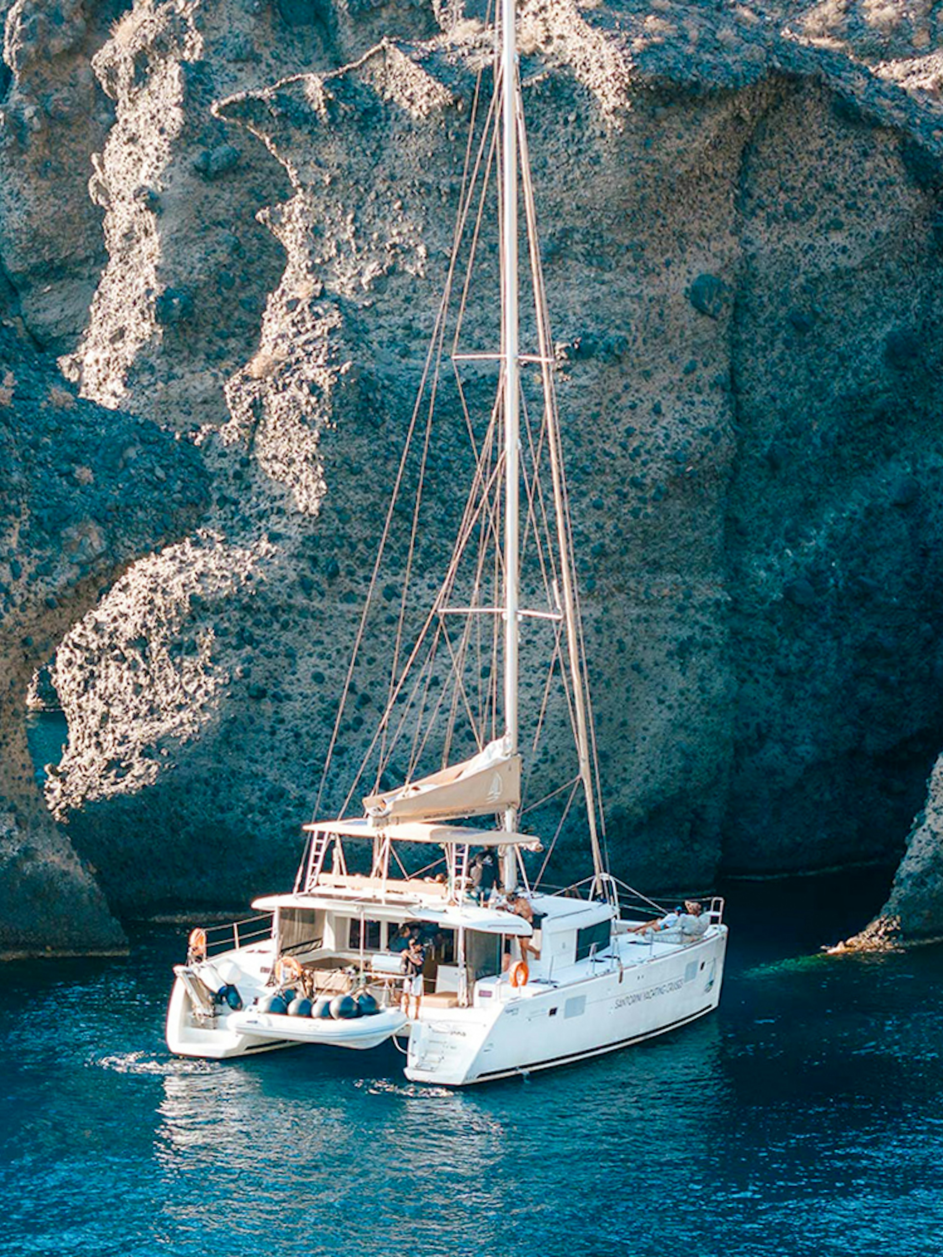 Catamaran sailing near rocky cliffs in Santorini, Greece.