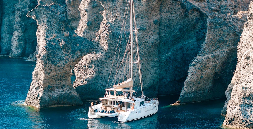 Catamaran sailing near rocky cliffs in Santorini, Greece.