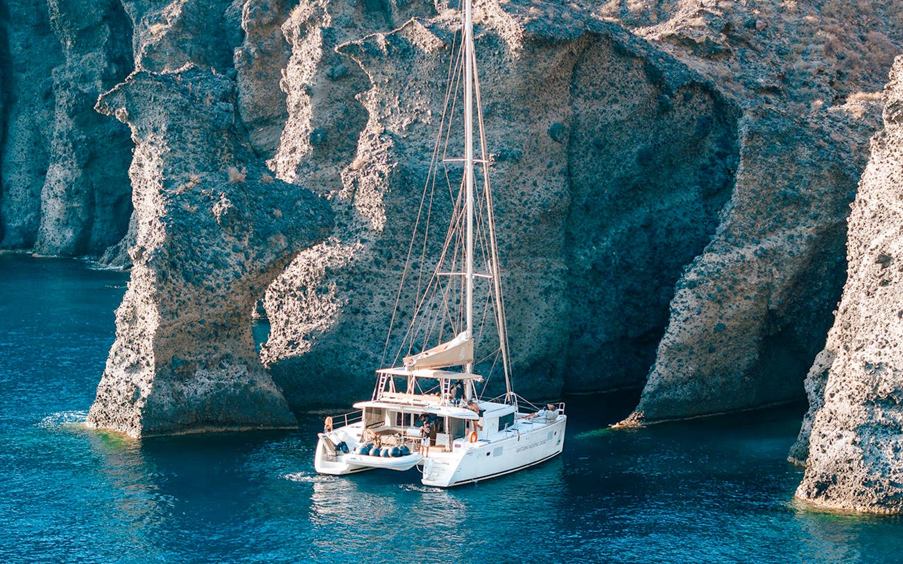 Catamaran sailing near rocky cliffs in Santorini, Greece.