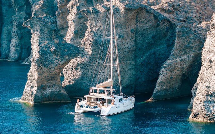 Catamaran sailing near rocky cliffs in Santorini, Greece.