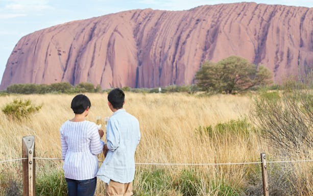 Couple enjoying sparkling wine with view of Uluru at sunset.