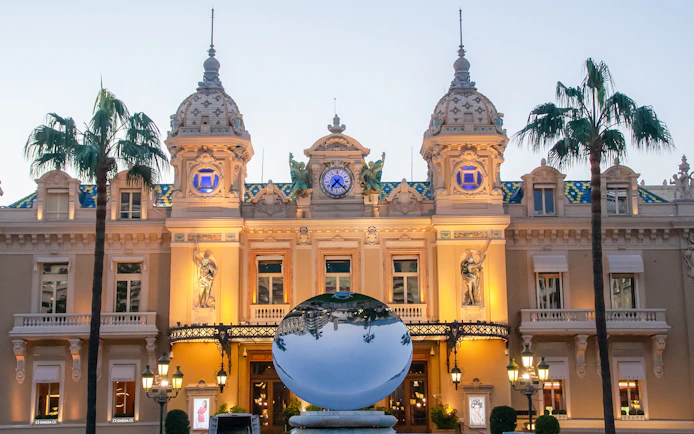 Monte Carlo Casino facade with reflective sculpture and palm trees.