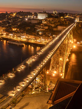 Pilar 7 Bridge illuminated at night with cityscape in the background, Lisbon, Portugal.
