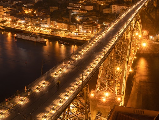 Pilar 7 Bridge illuminated at night with cityscape in the background, Lisbon, Portugal.