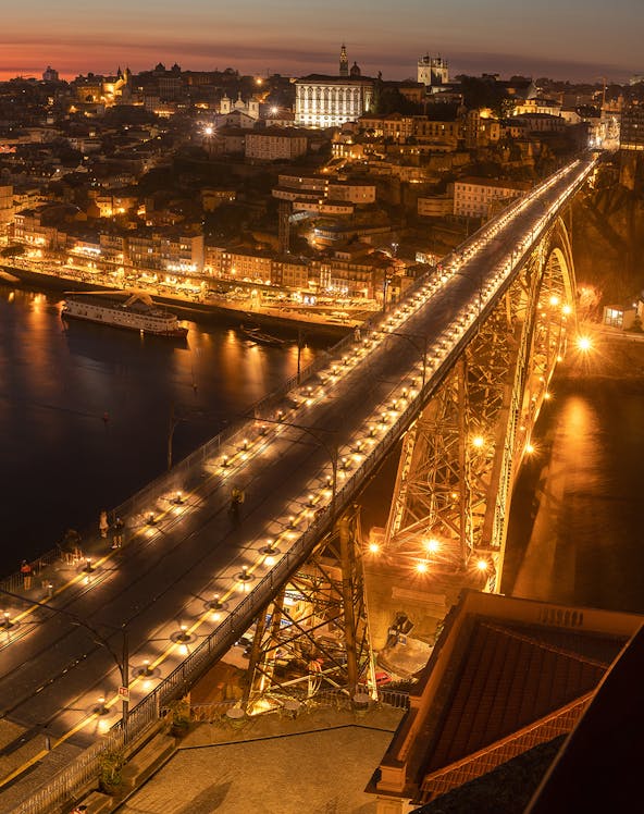 Pilar 7 Bridge illuminated at night with cityscape in the background, Lisbon, Portugal.