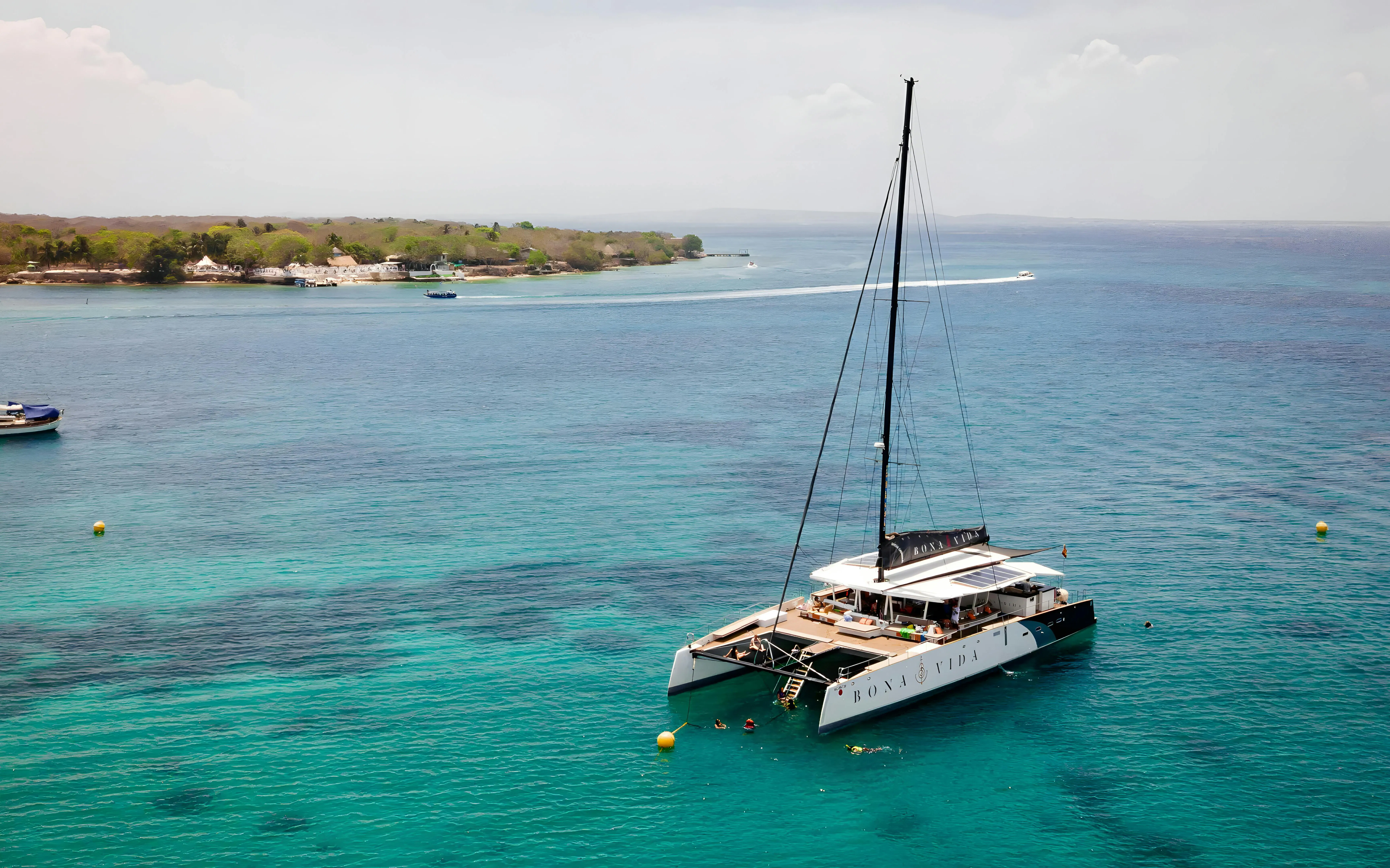 Catamaran anchored near Rosario Islands with people swimming in clear blue water.