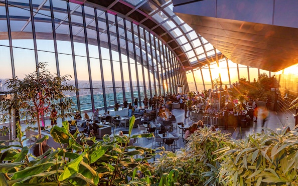 Sky Garden London evening view with people dining and cityscape backdrop.