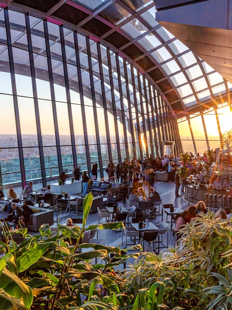 Sky Garden London evening view with people dining and cityscape backdrop.