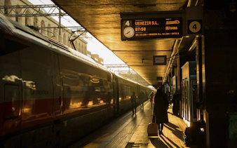 Train station in Italy with travelers and a train during sunset.
