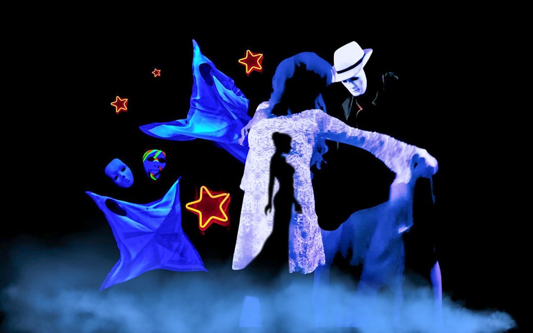 Performers in black light theatre with glowing masks and stars, Prague.