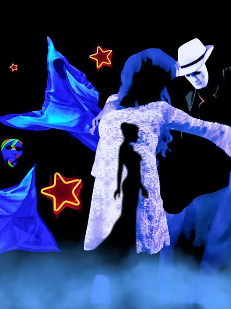Performers in black light theatre with glowing masks and stars, Prague.