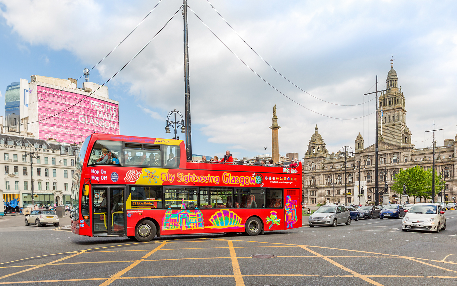 Open-top sightseeing bus in George Square, Glasgow, with City Chambers in the background.