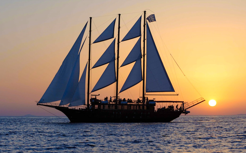 Sailing ship at sunset near volcanic islands.