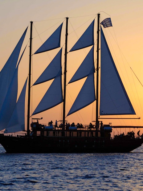 Sailing ship at sunset near volcanic islands.