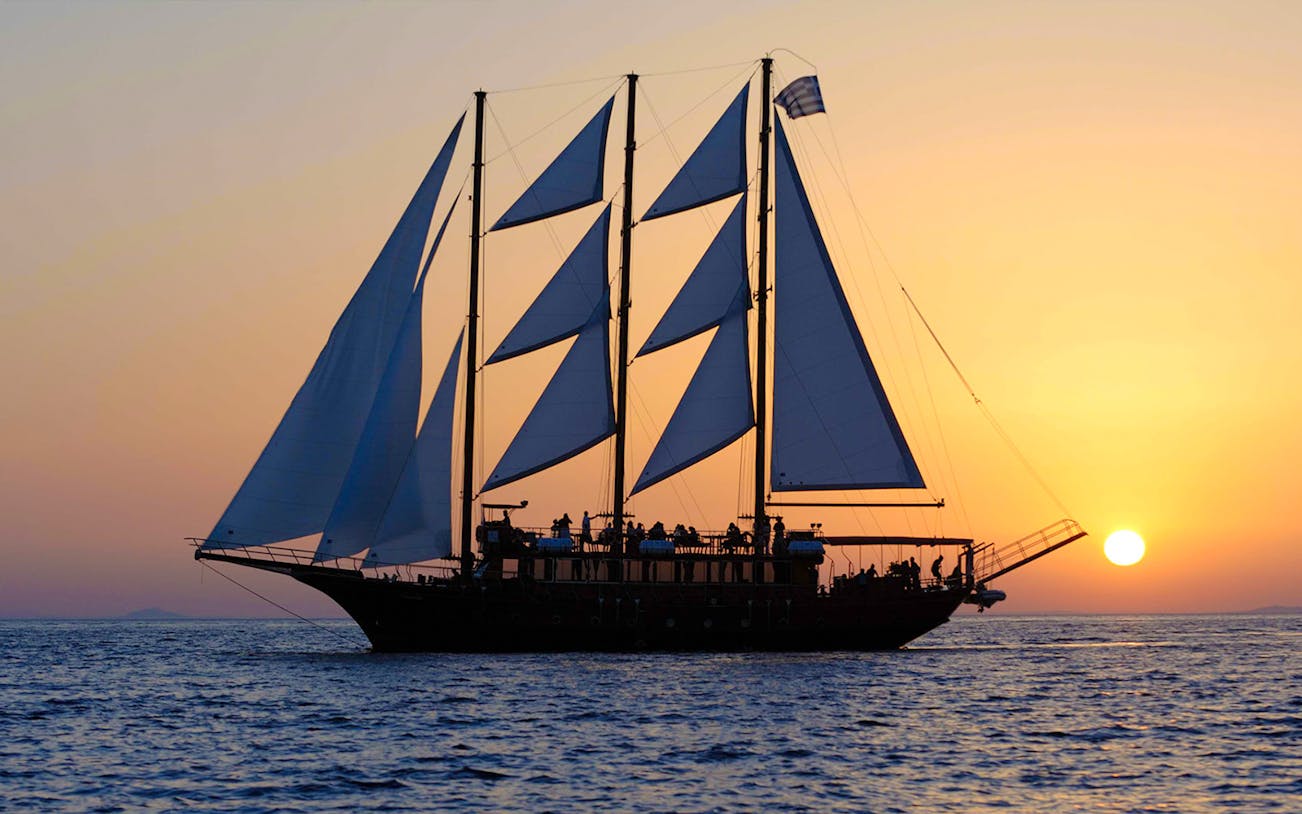 Sailing ship at sunset near volcanic islands.