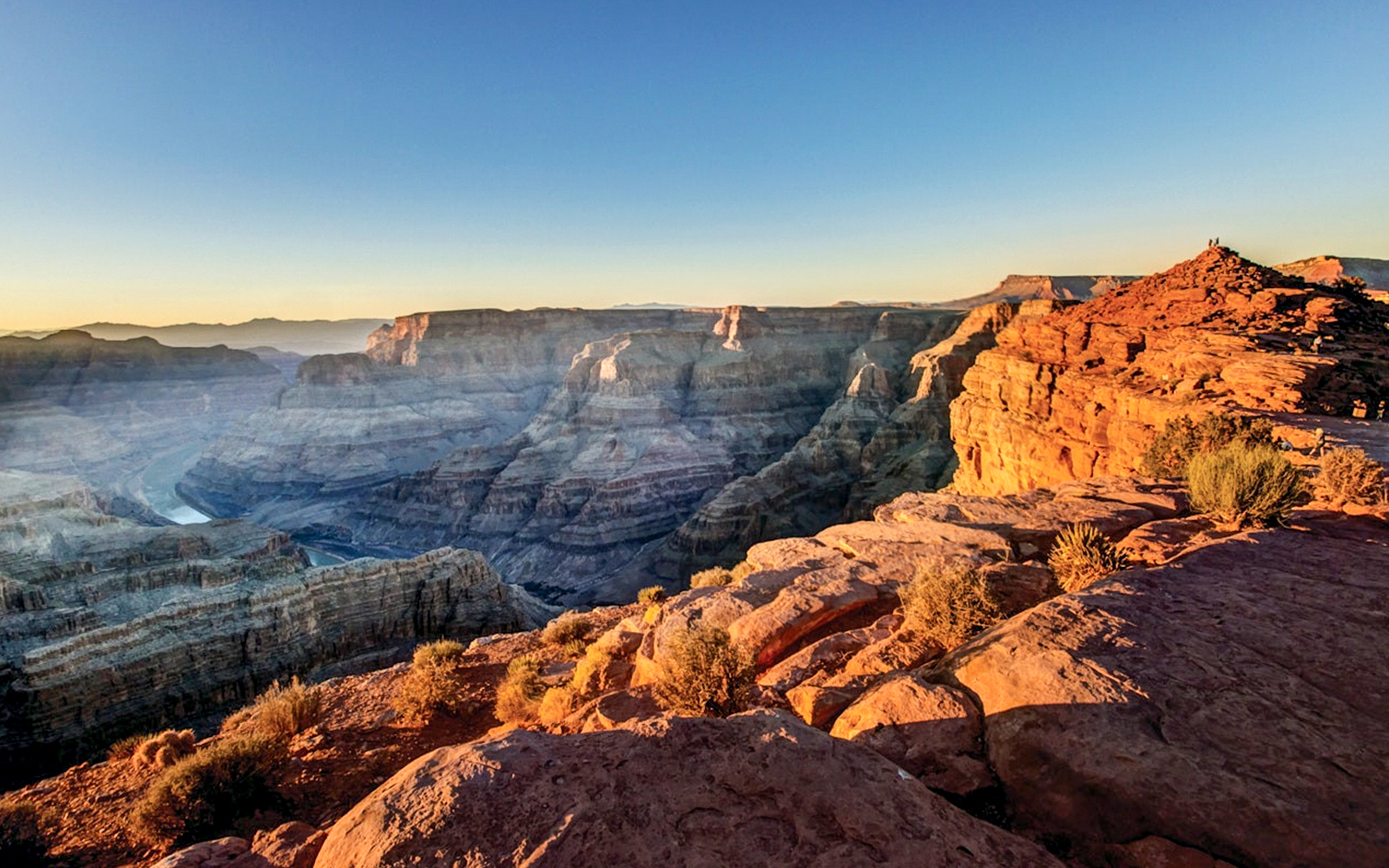 Tourists viewing the Grand Canyon West Rim from an observation point with a clear sky.