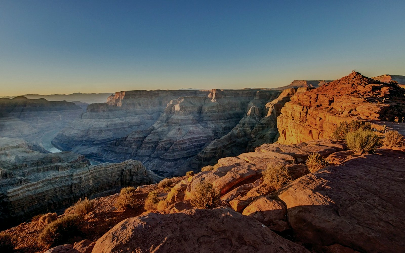 Tourists viewing the Grand Canyon West Rim from an observation point with a clear sky.