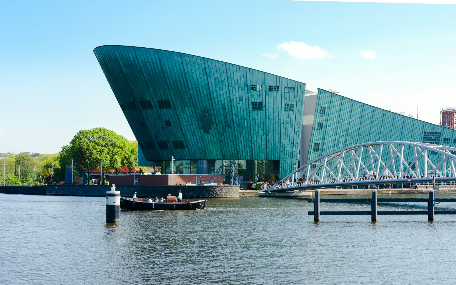 NEMO Science Museum exterior with canal and pedestrian bridge in Amsterdam.