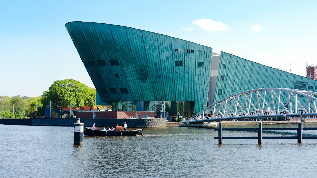 NEMO Science Museum exterior with canal and pedestrian bridge in Amsterdam.