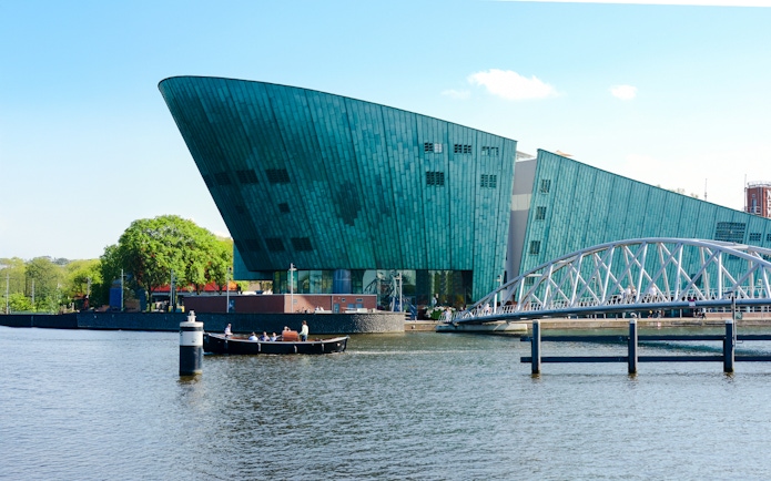 NEMO Science Museum exterior with canal and pedestrian bridge in Amsterdam.