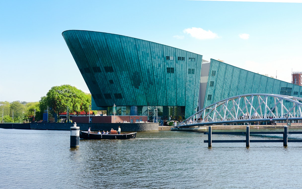 NEMO Science Museum exterior with canal and pedestrian bridge in Amsterdam.